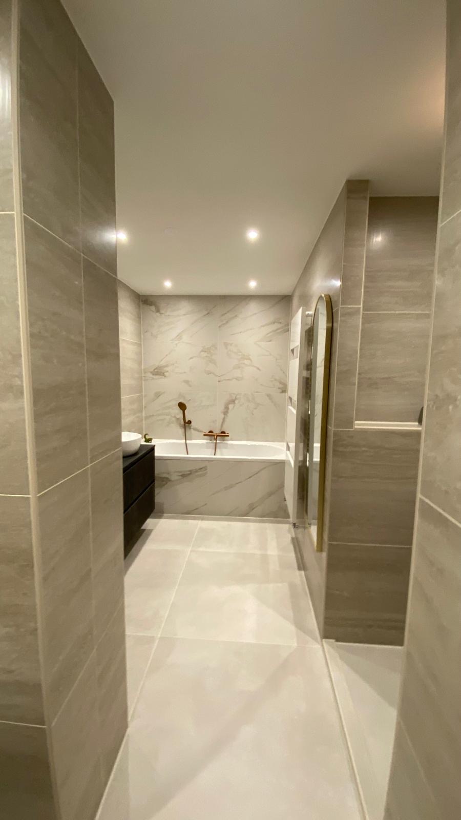 Lichte badkamer met ligbad en marmerlook wandtegels, gemaakt door 050 Montage.