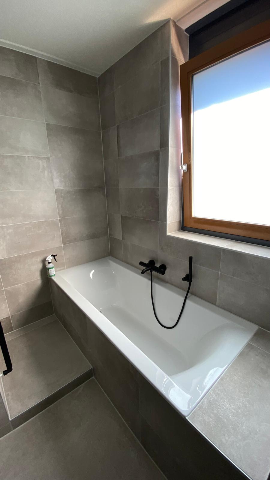Badkamer met ligbad, houten wastafelmeubel en zwarte douchewand.