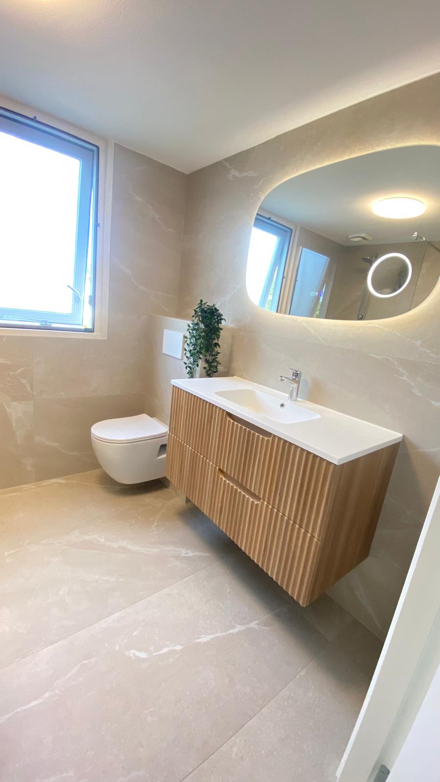 Lichte badkamer met een houten wastafelmeubel en verlichte spiegel.