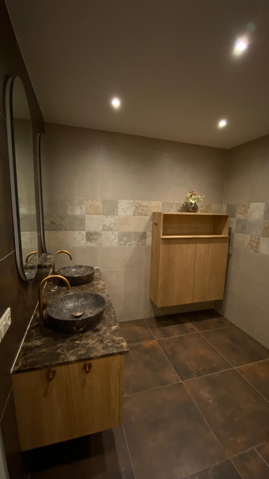 Badkamer met een dubbel natuurstenen wastafelblad en warme houten meubels.