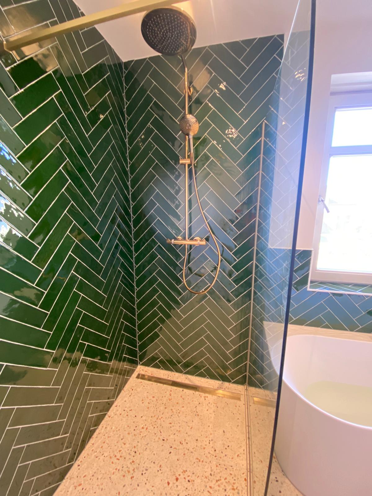 Inloopdouche met groene visgraattegels, glazen wand en goudkleurige douche, gemaakt door 050 Montage.