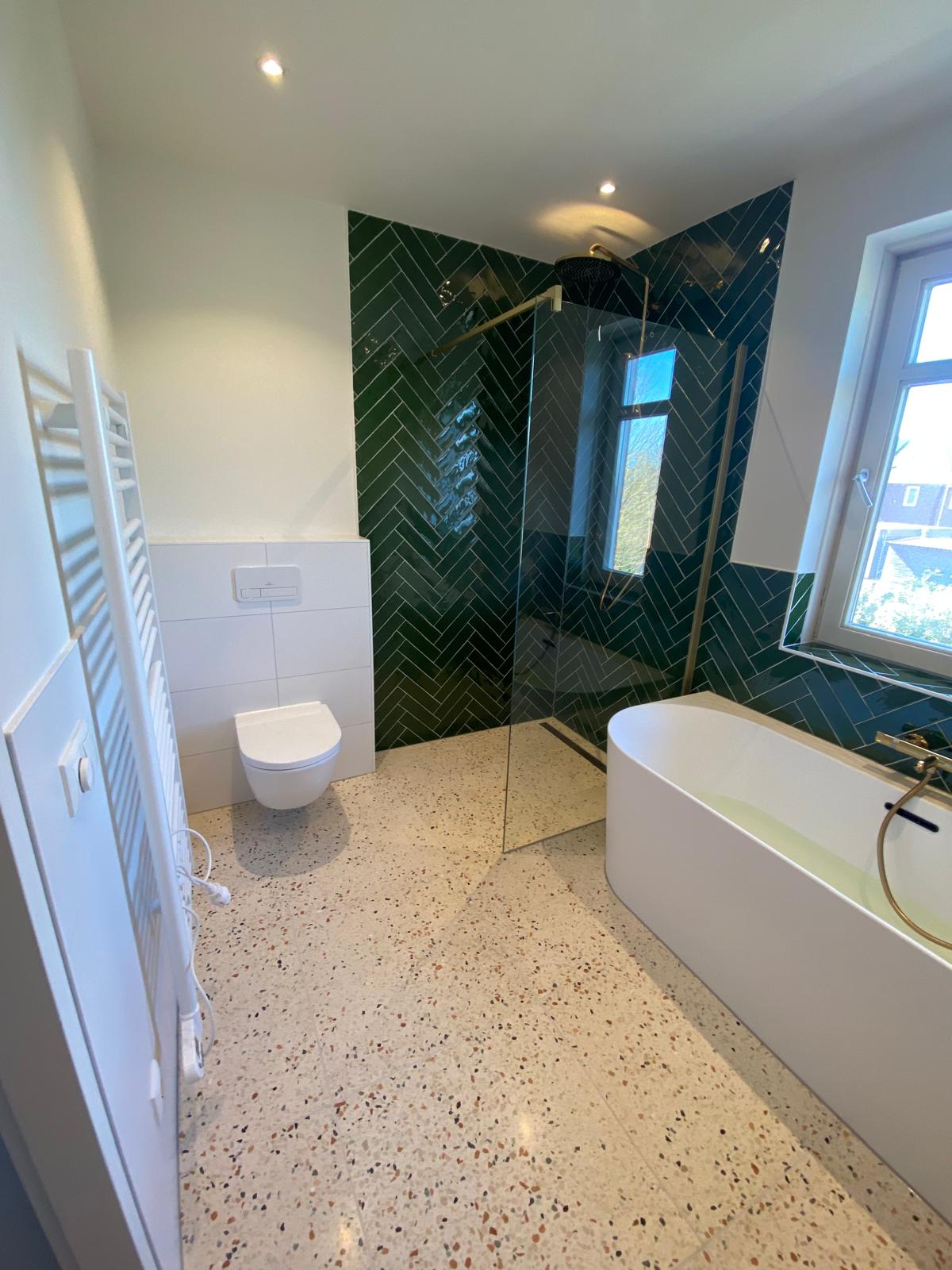 Badkamer met vrijstaand bad en groene visgraattegels in de douche.